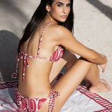 This image features the Chloe Granate Cheeky Tie Side Bikini Bottom by Mar de Lua, designed in a vivid granate red with a distinctive palm tree print. The bikini bottom is crafted with cheeky coverage and includes ruched back details for a flattering fit, along with adjustable rope-tie sides for an secure and adjustable waist.