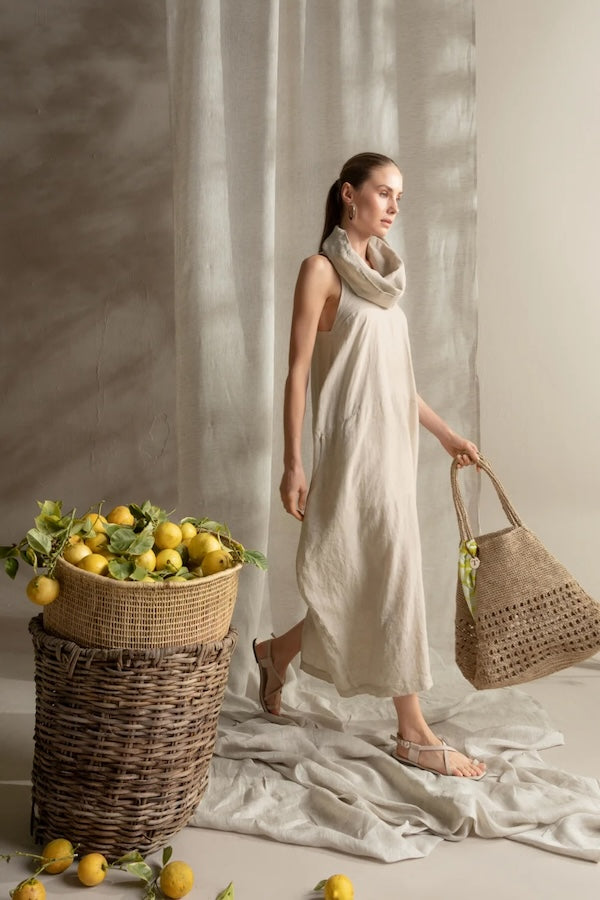 Woman in a beige dress holding a woven bag next to a basket of lemons.