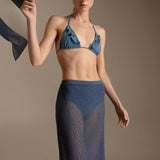 Woman wearing a blue bikini top and mesh maxi skirt against a neutral background.