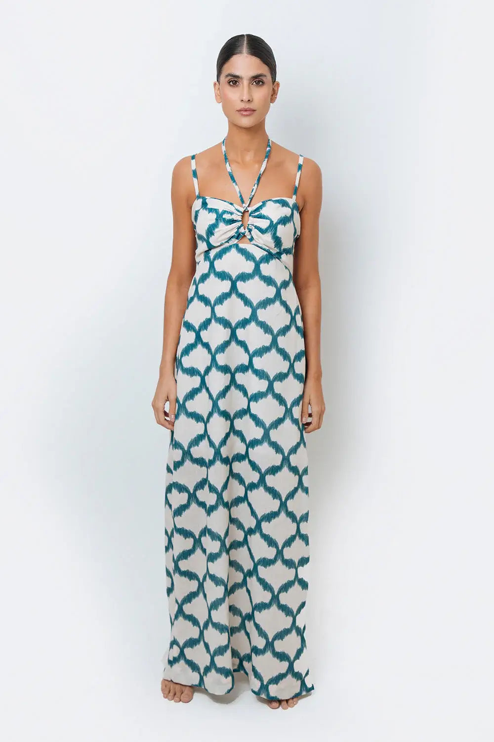 A model wearing a halter neck, sleeveless, maxi-length dress with a geometric pattern in teal and cream colors.
