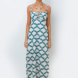 A model wearing a halter neck, sleeveless, maxi-length dress with a geometric pattern in teal and cream colors.