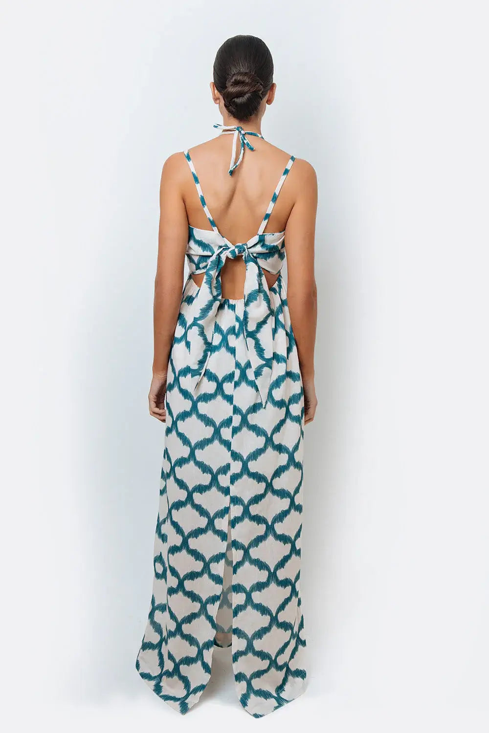 A model wearing a halter neck, sleeveless, maxi-length dress with a geometric pattern in teal and cream colors.