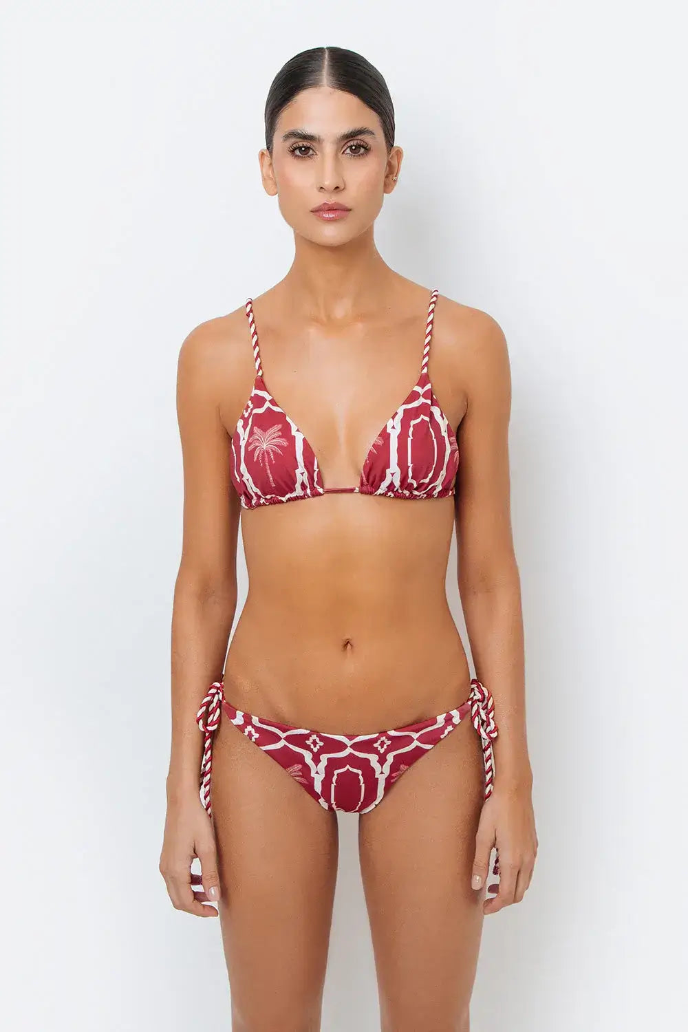 This image features the Chloe Granate Cheeky Tie Side Bikini Bottom by Mar de Lua, designed in a vivid granate red with a distinctive palm tree print. The bikini bottom is crafted with cheeky coverage and includes ruched back details for a flattering fit, along with adjustable rope-tie sides for an secure and adjustable waist.