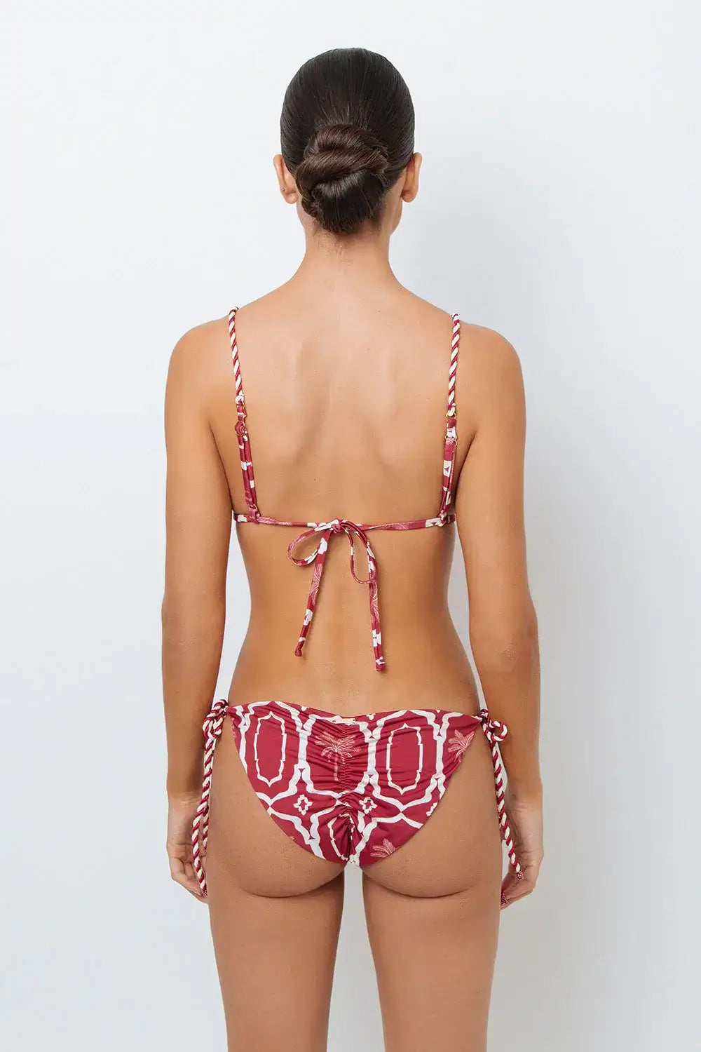 This image features the Chloe Granate Cheeky Tie Side Bikini Bottom by Mar de Lua, designed in a vivid granate red with a distinctive palm tree print. The bikini bottom is crafted with cheeky coverage and includes ruched back details for a flattering fit, along with adjustable rope-tie sides for an secure and adjustable waist.