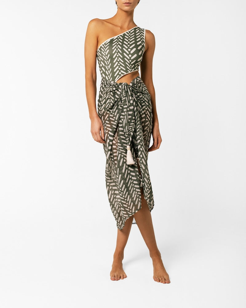 Woman wearing a green and white patterned one-shoulder one-piece bikini with a matching shawl on a white background.