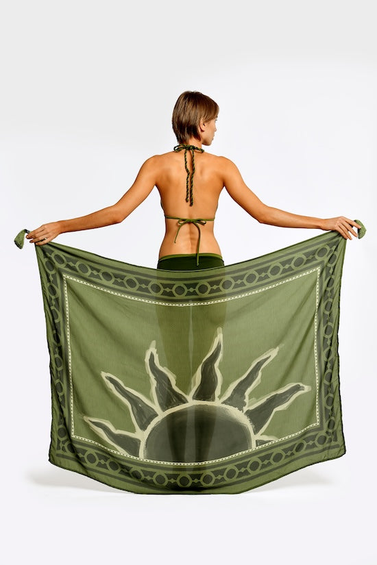 Woman holding a green sarong with a sun design on a white background.