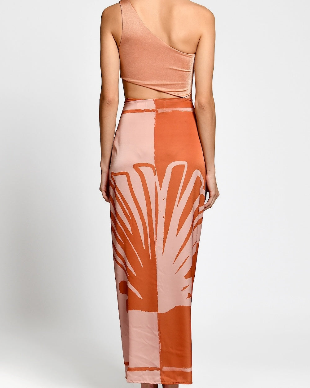 Woman wearing a one-shoulder dress with a palm leaf pattern on a white background.