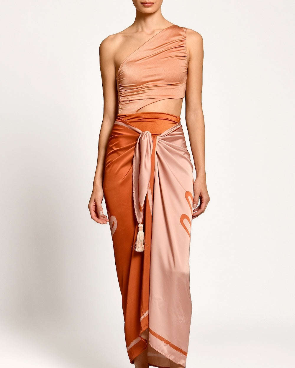 Woman wearing a peach and orange one-shoulder dress with a matching skirt on a white background.