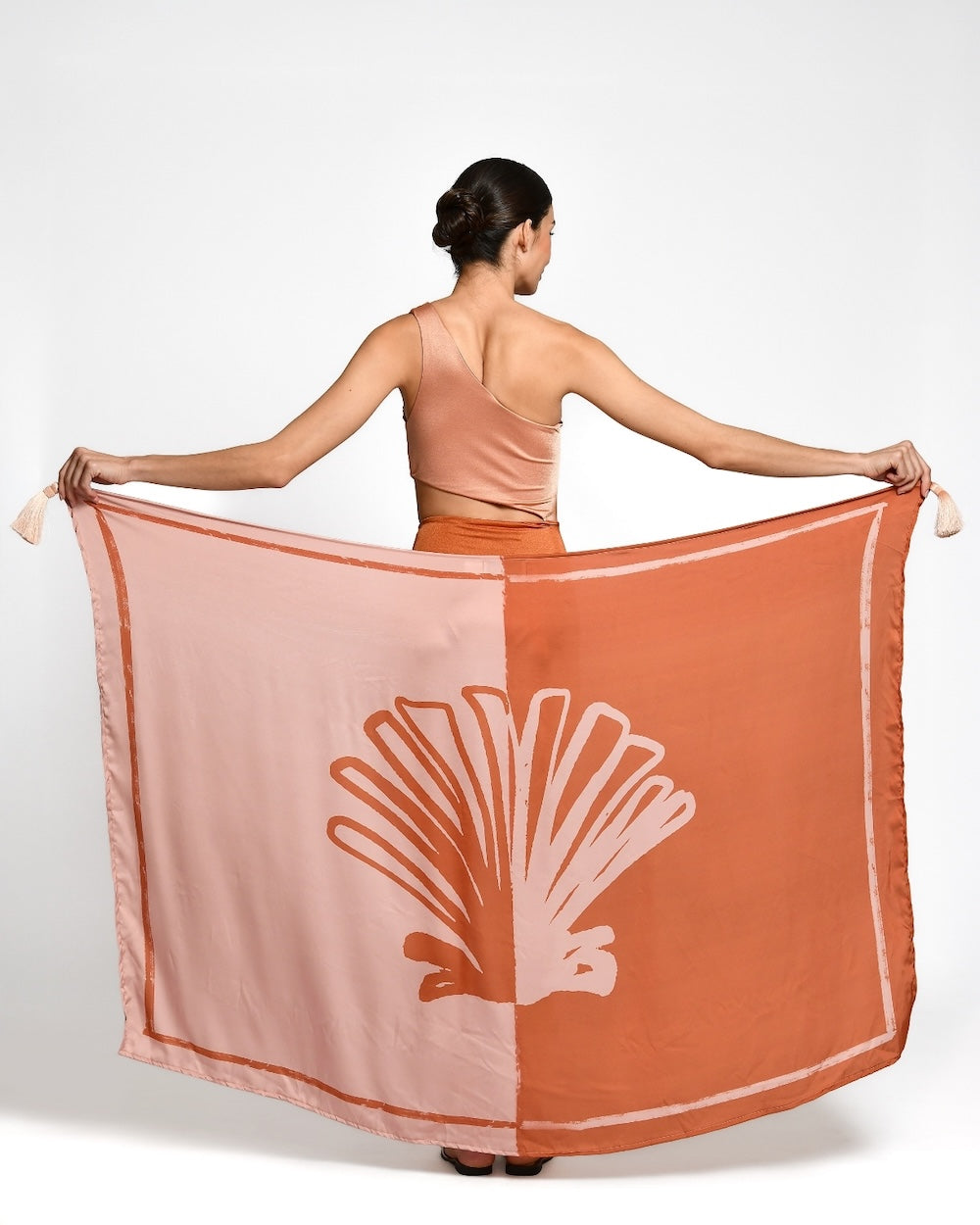 Woman holding a large pink and orange scarf with a shell design on a white background.