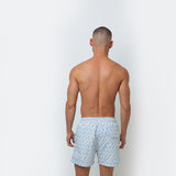 Man wearing light blue patterned swim shorts against a white background.