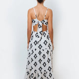 A woman modeling a sleeveless, spaghetti-strap maxi dress with a geometric black and white pattern, featuring cut-out side detail with an adjustable back-tie.
