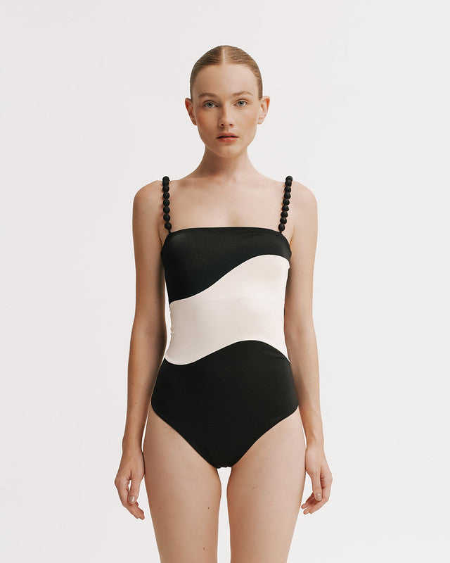 Woman wearing a black and white swimsuit with braided straps on a plain background
