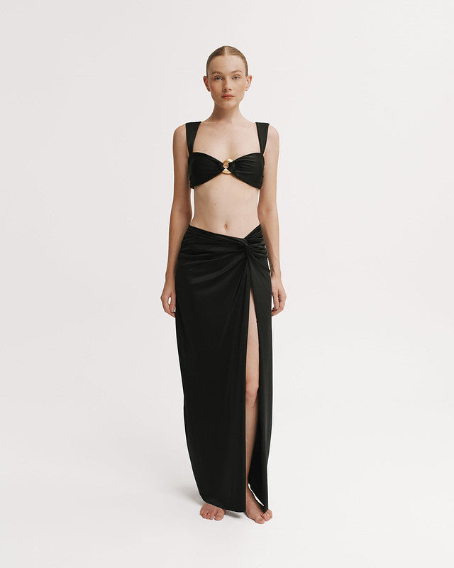 Woman wearing a black dress with a high slit on a white background.