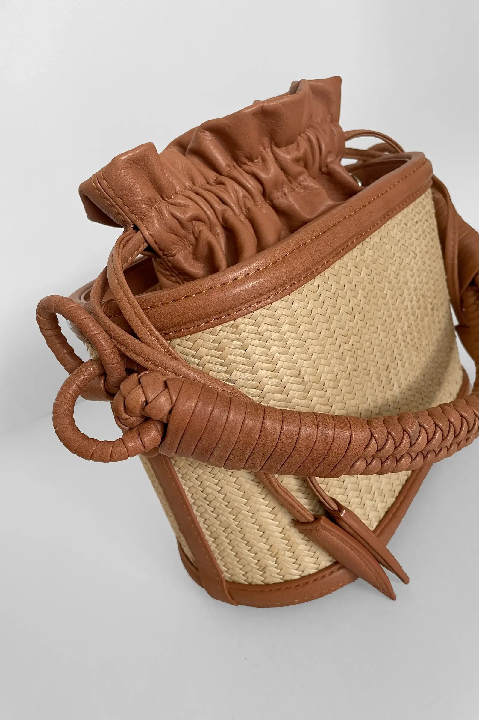 Brown leather and straw handbag on a light gray background.