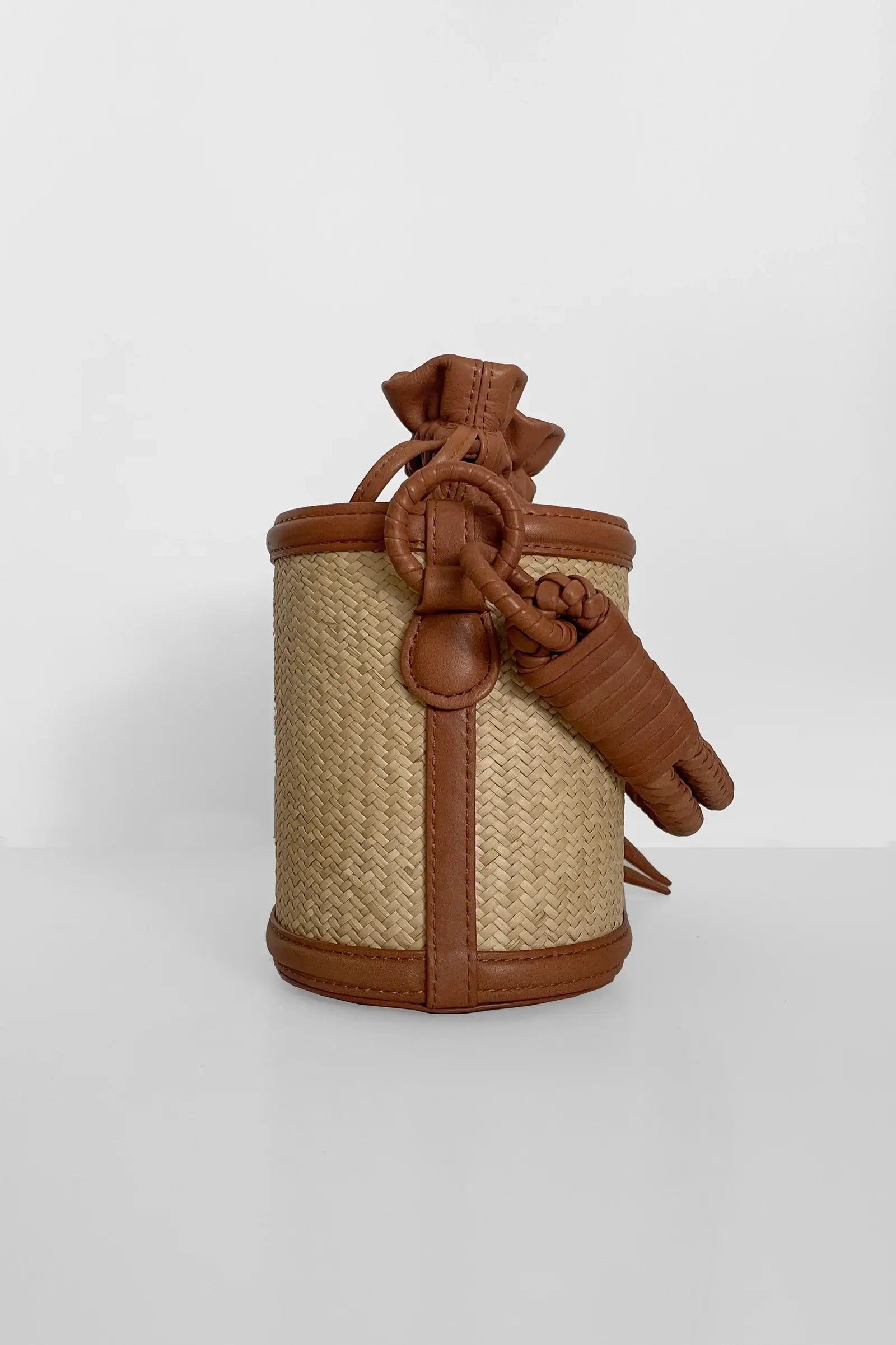 Small woven basket with brown leather straps and knot on a white background.