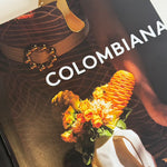 Close up image of a mushroom-shaped bookmark in gold, on a book called, "Colombiana." The purpose of this image is to highlight the bookmark, which is handmade by PAJAROLIMON.