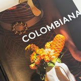 Close up image of a mushroom-shaped bookmark in gold, on a book called, "Colombiana." The purpose of this image is to highlight the bookmark, which is handmade by PAJAROLIMON.