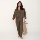 Woman wearing an olive green top and pants set with a matching jacket holding a beige bag on a white background.