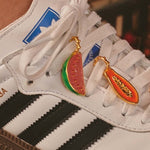 A close-up of a shoe with gold-plated shoelace charms of a papaya and a watermelon.