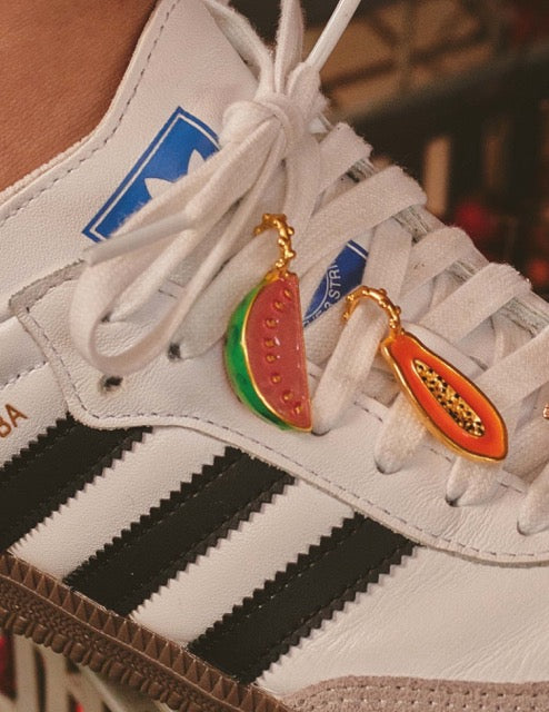 A close-up of a shoe with gold-plated shoelace charms of a papaya and a watermelon.