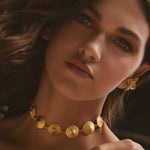 Woman wearing gold jewelry including a necklace, earrings, and ring.