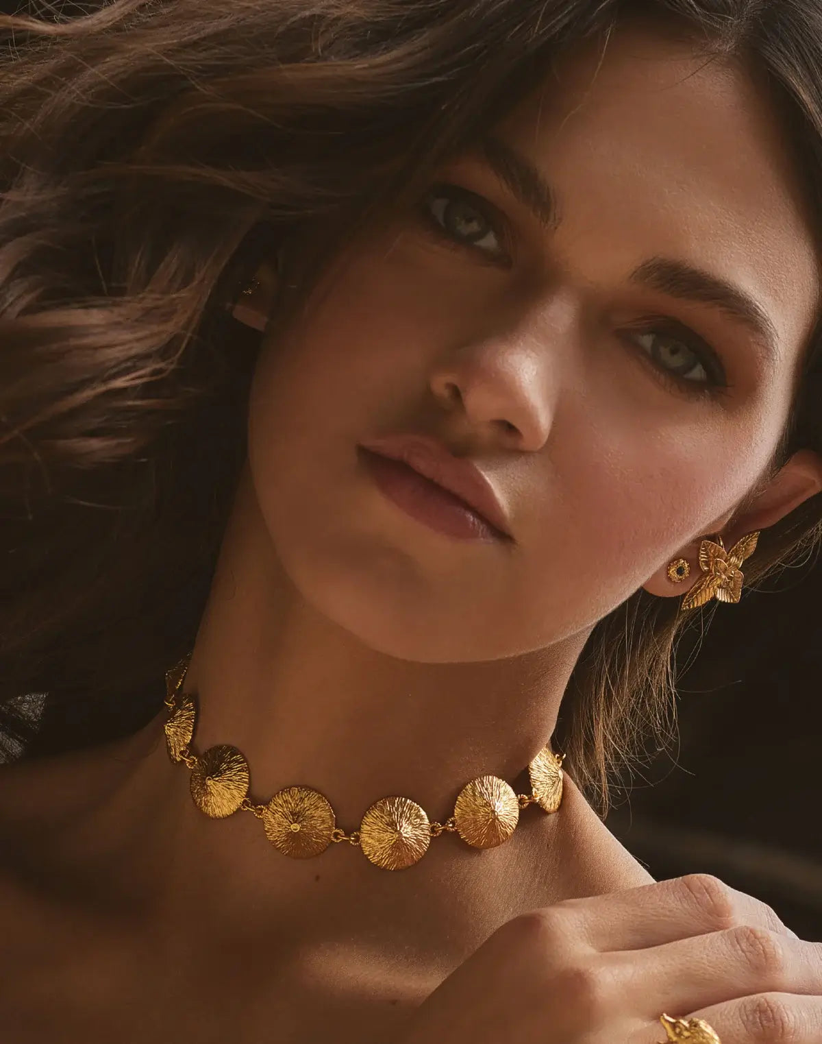 Woman wearing gold jewelry including a necklace, earrings, and ring.