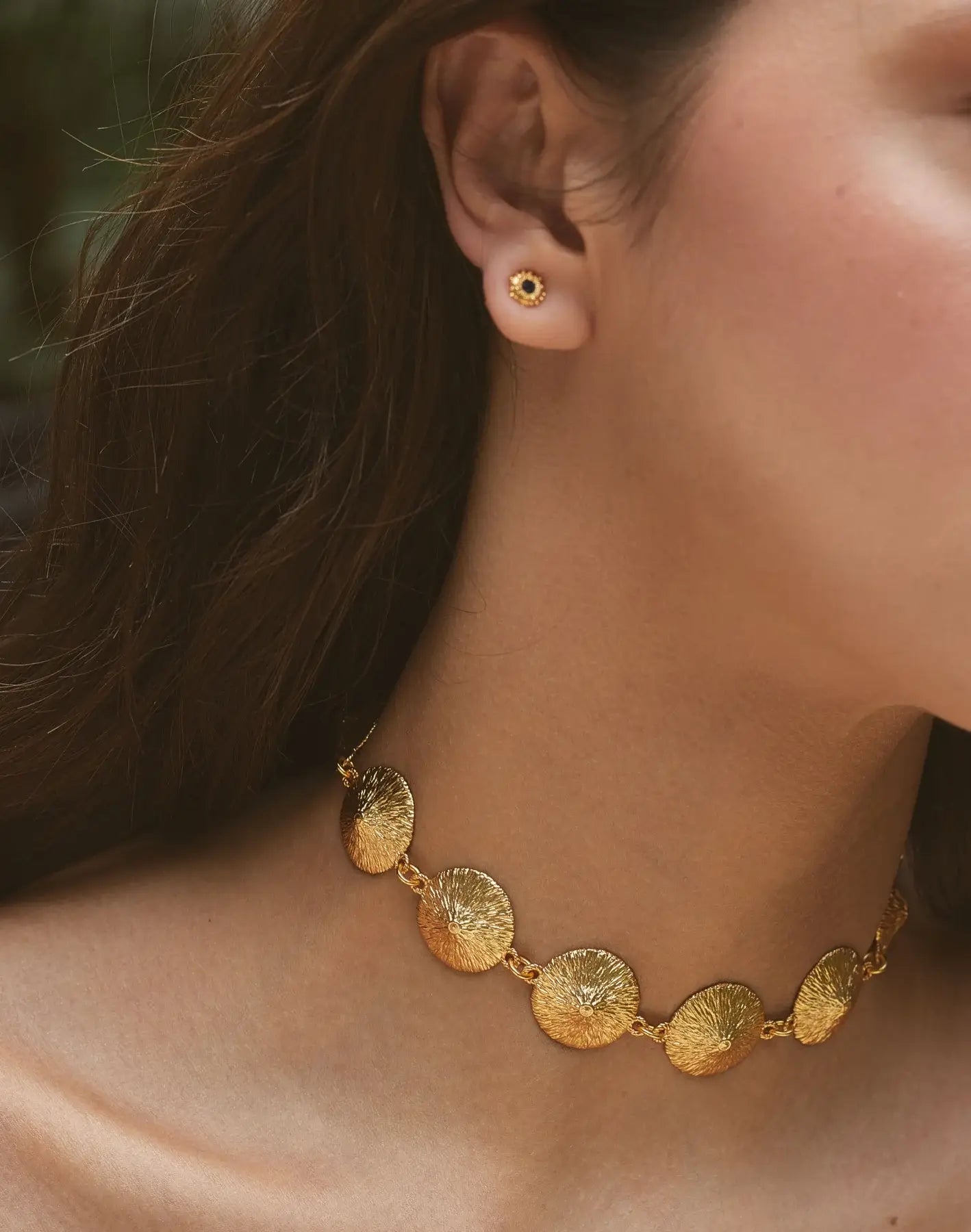Close-up of a person wearing a gold necklace and earrings.