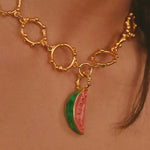 Gold necklace with a watermelon charm on a person's neck.
