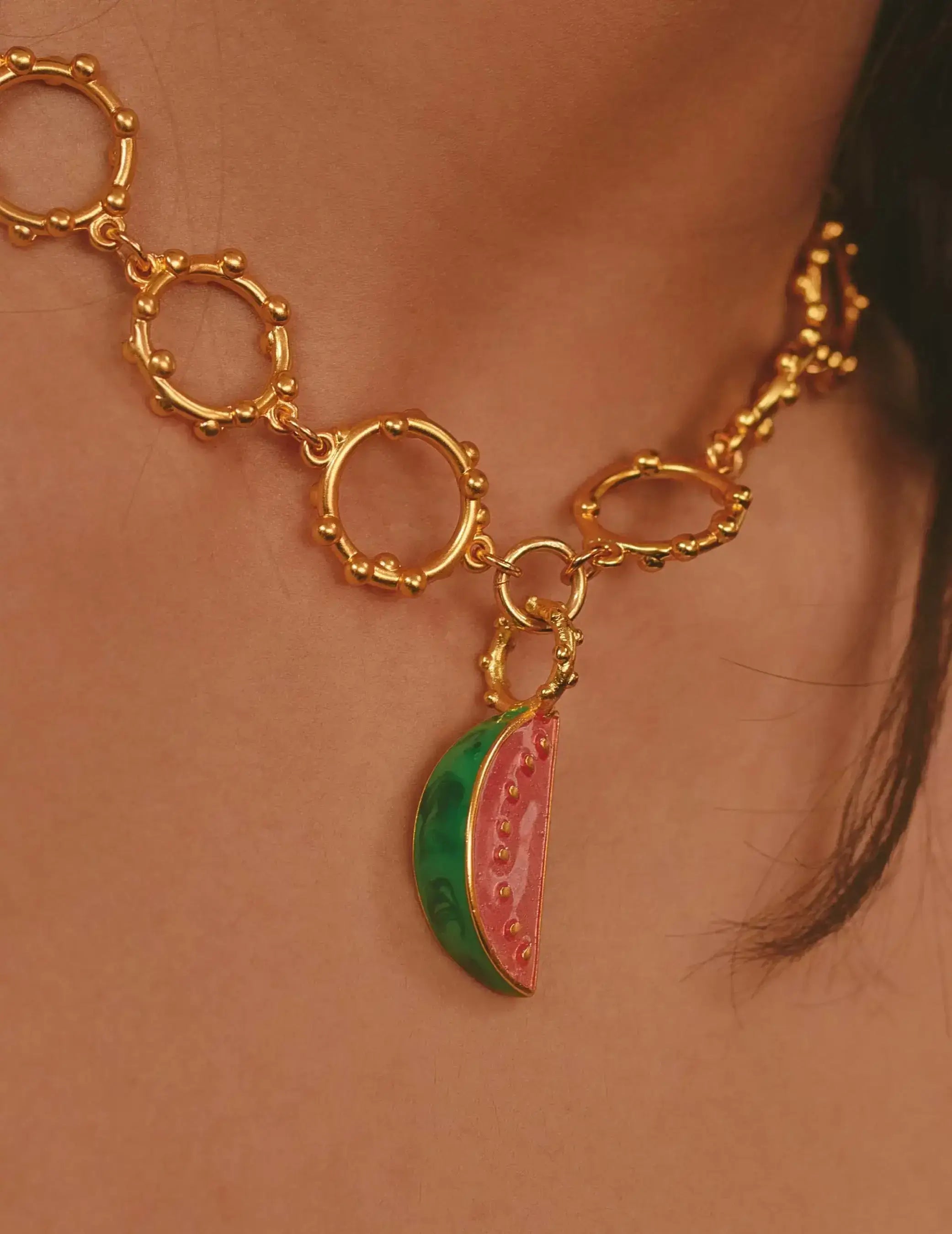 Gold necklace with a watermelon charm on a person's neck.