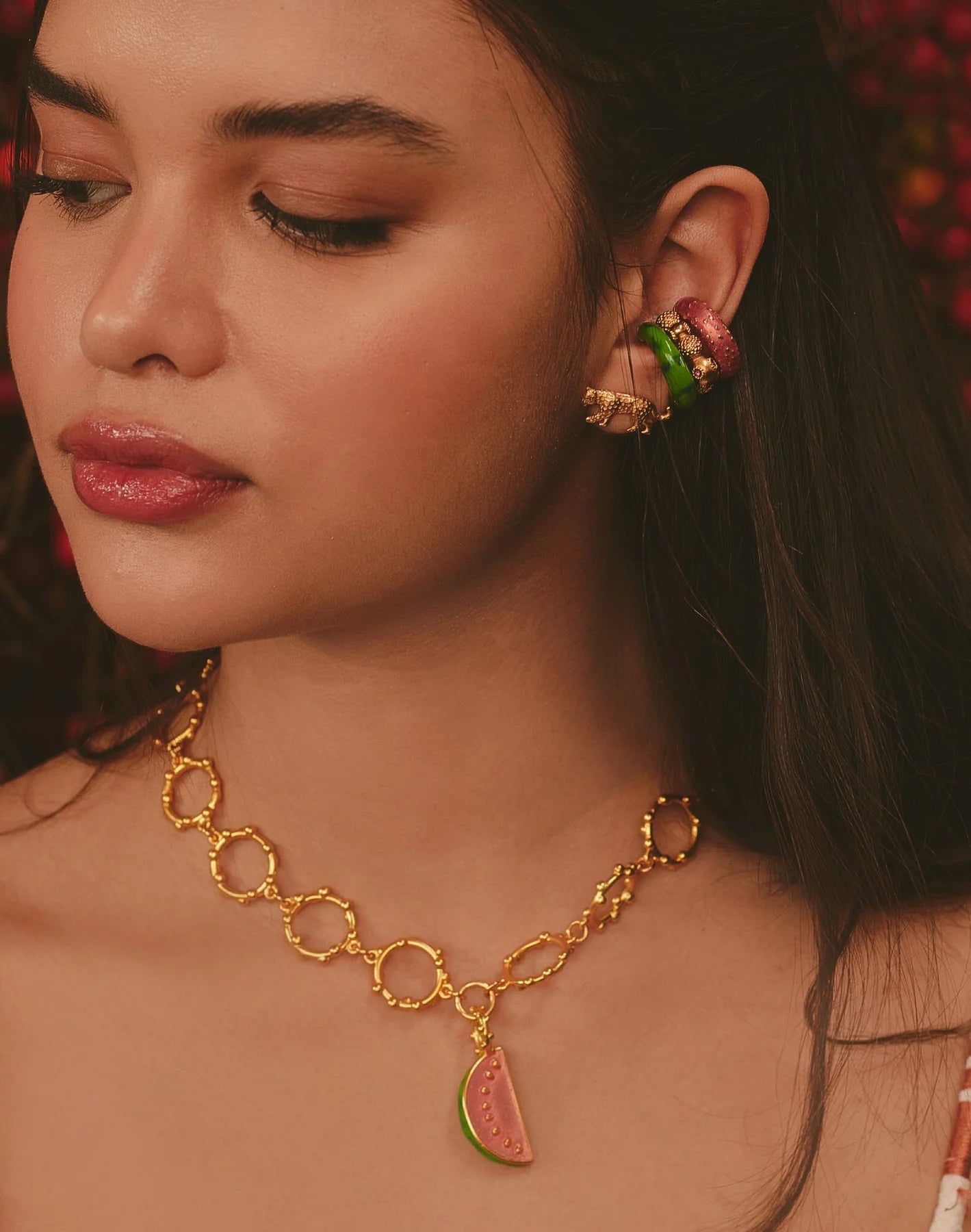Close-up of a woman wearing gold necklace with a watermelon charm.