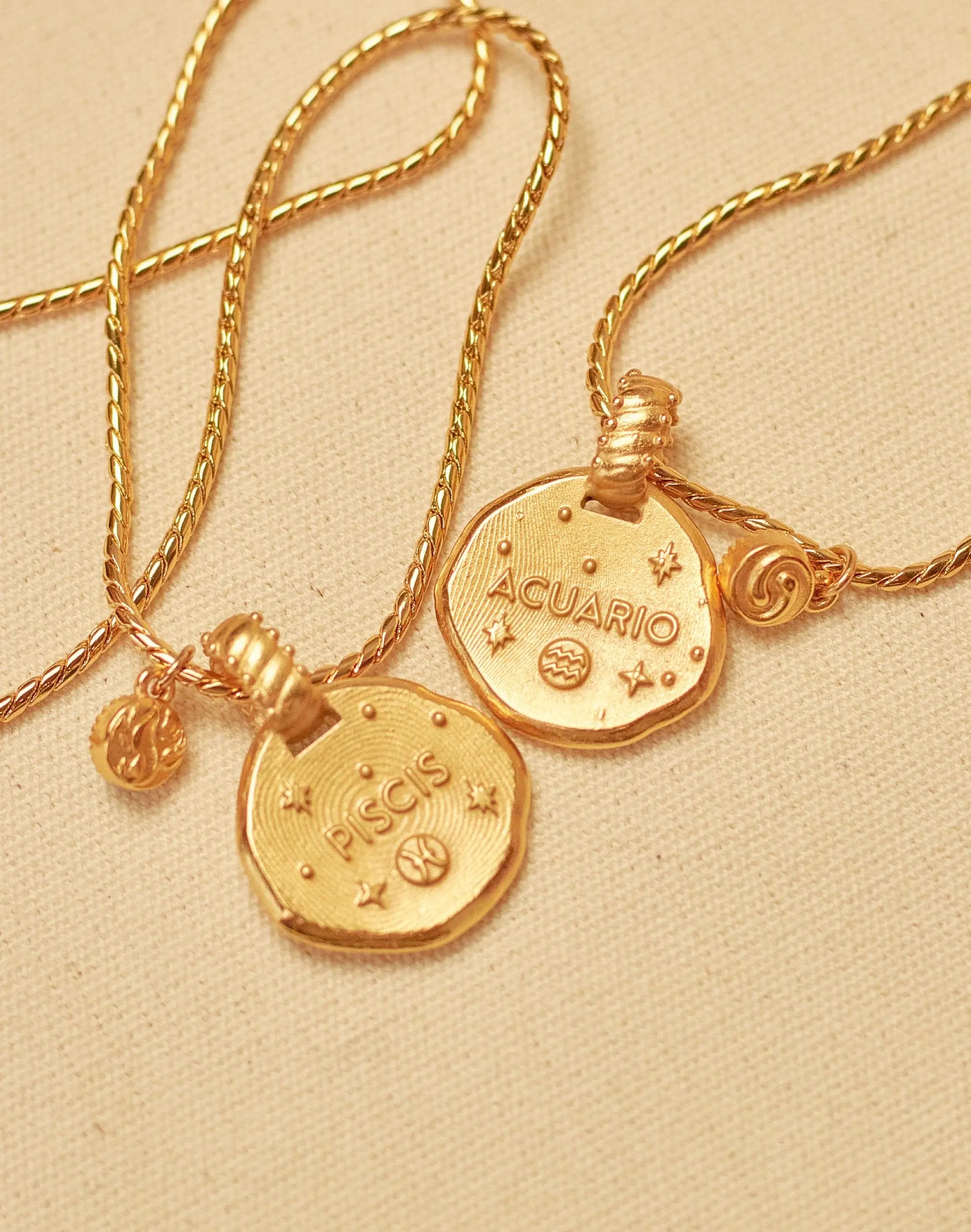 A collection of 24k gold-plated necklaces with different zodiac sign pendants, each accompanied by a natural stone charm, displayed on a beige background.