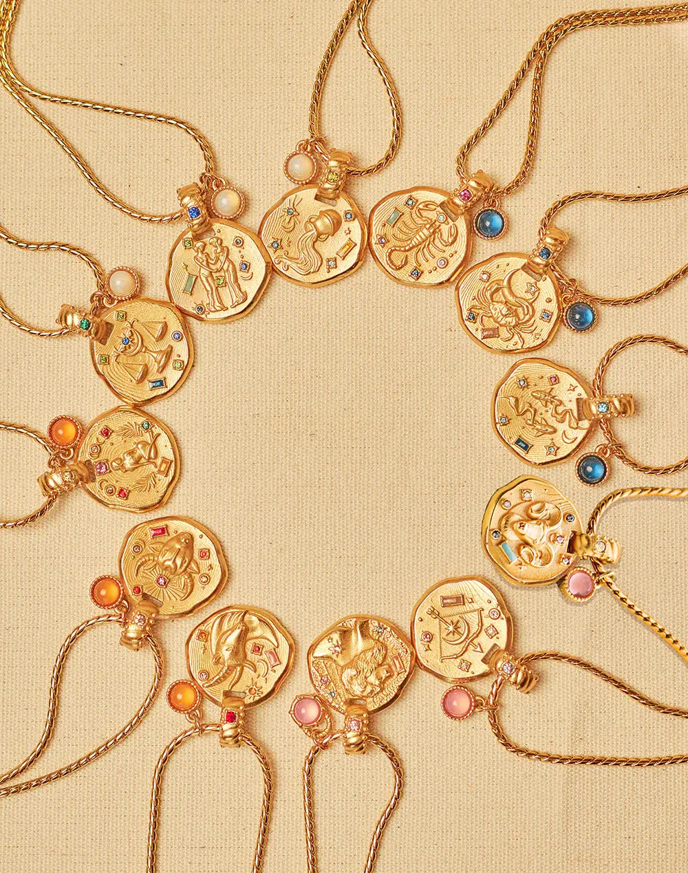 A collection of 24k gold-plated necklaces with different zodiac sign pendants, each accompanied by a natural stone charm, displayed on a beige background.