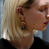 Close-up of a person wearing gold statement earrings with gold/silver cuffs in a blurred background.