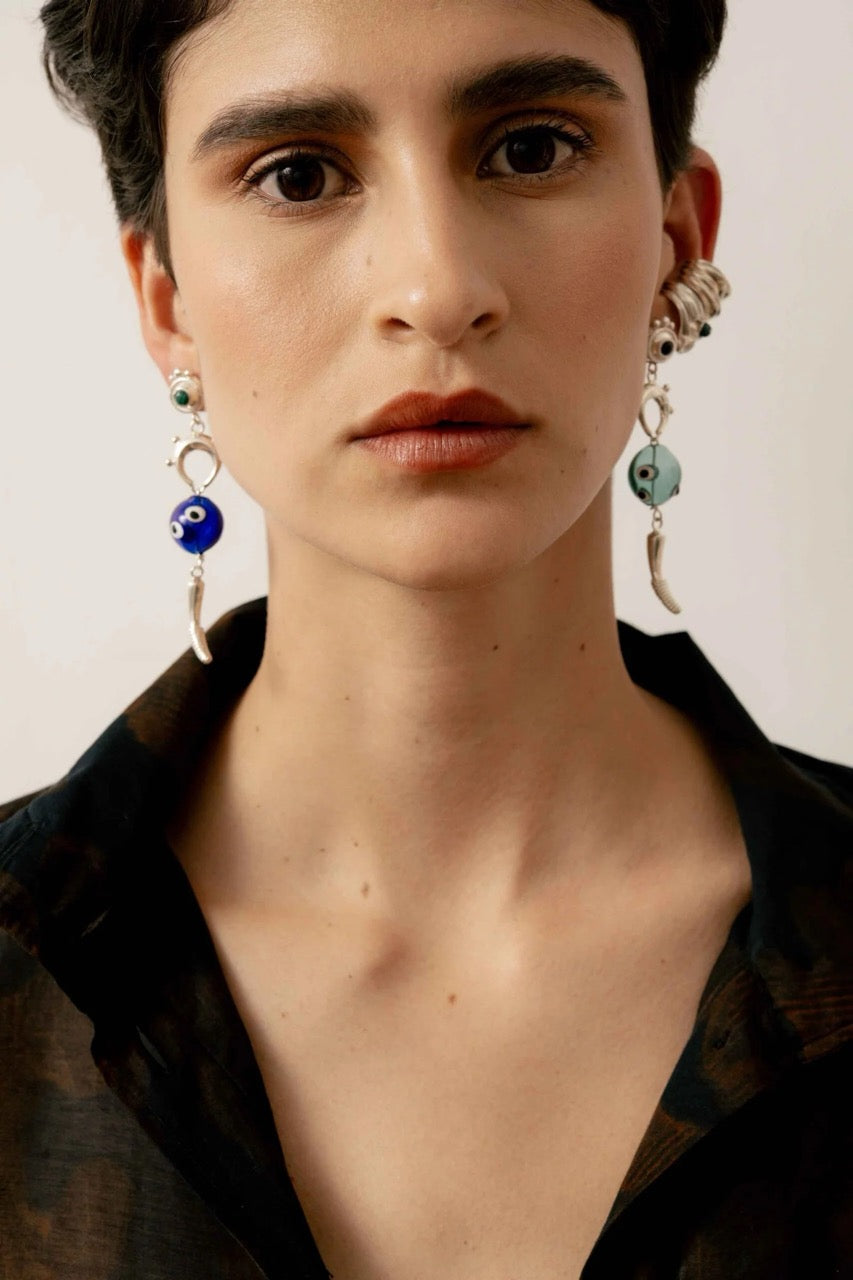 Close-up of a person wearing silver earrings with dark and light blue accents in front of neutral background.
