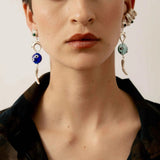 Close-up of a person wearing silver earrings with dark and light blue accents in front of neutral background.