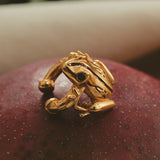 A gold-plated earcuff of a Coqui frog, displayed on a red surface.