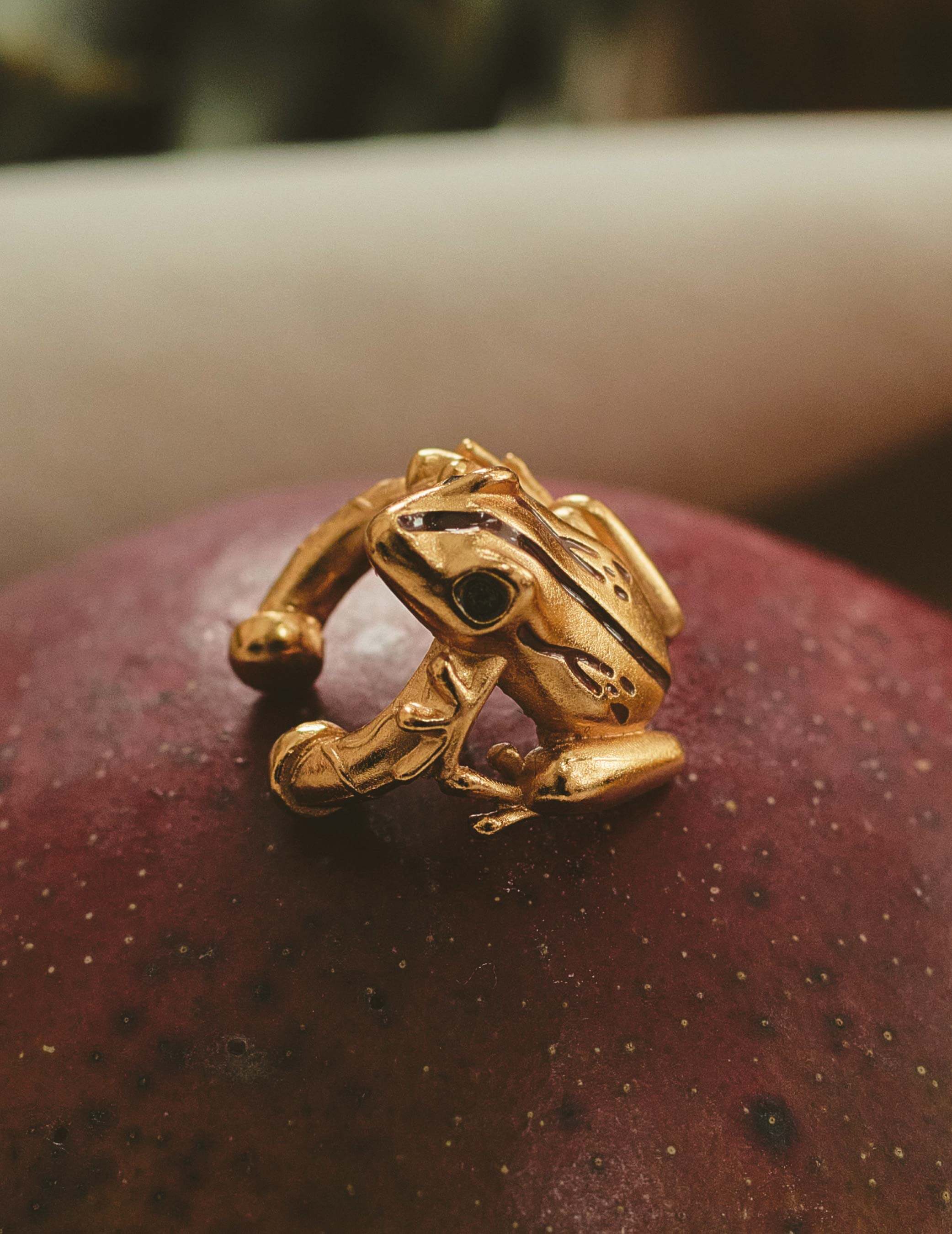 A gold-plated earcuff of a Coqui frog, displayed on a red surface.