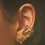 A close-up of a pair of gold-plated palm stud earrings and a Coui frog earcuff.