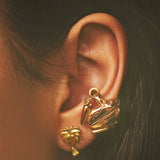 A close-up of a pair of gold-plated palm stud earrings and a Coui frog earcuff.
