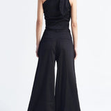 Image of a woman wearing a one shoulder top with matching pants in black. The image is set against a white background. The purpose of this image is to highlight the clothing by Encantadore because it's for sale at EVAMAIA boutique in Studio City, CA.