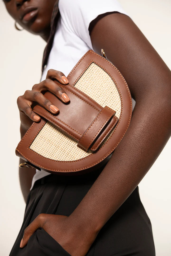 Person holding a brown leather handbag with beige accents against a plain background.