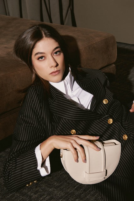 Woman in a pinstripe suit holding a beige handbag on a couch.