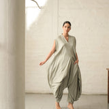 Woman wearing a green jumpsuit standing in a minimalistic room with white walls and tiled floor.
