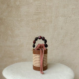 Small woven bucket bag with a handle on a textured beige background.