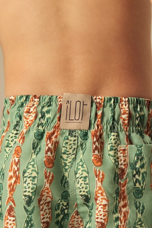 Green and orange fish-patterned swim shorts with a visible brand label on a person wearing them.