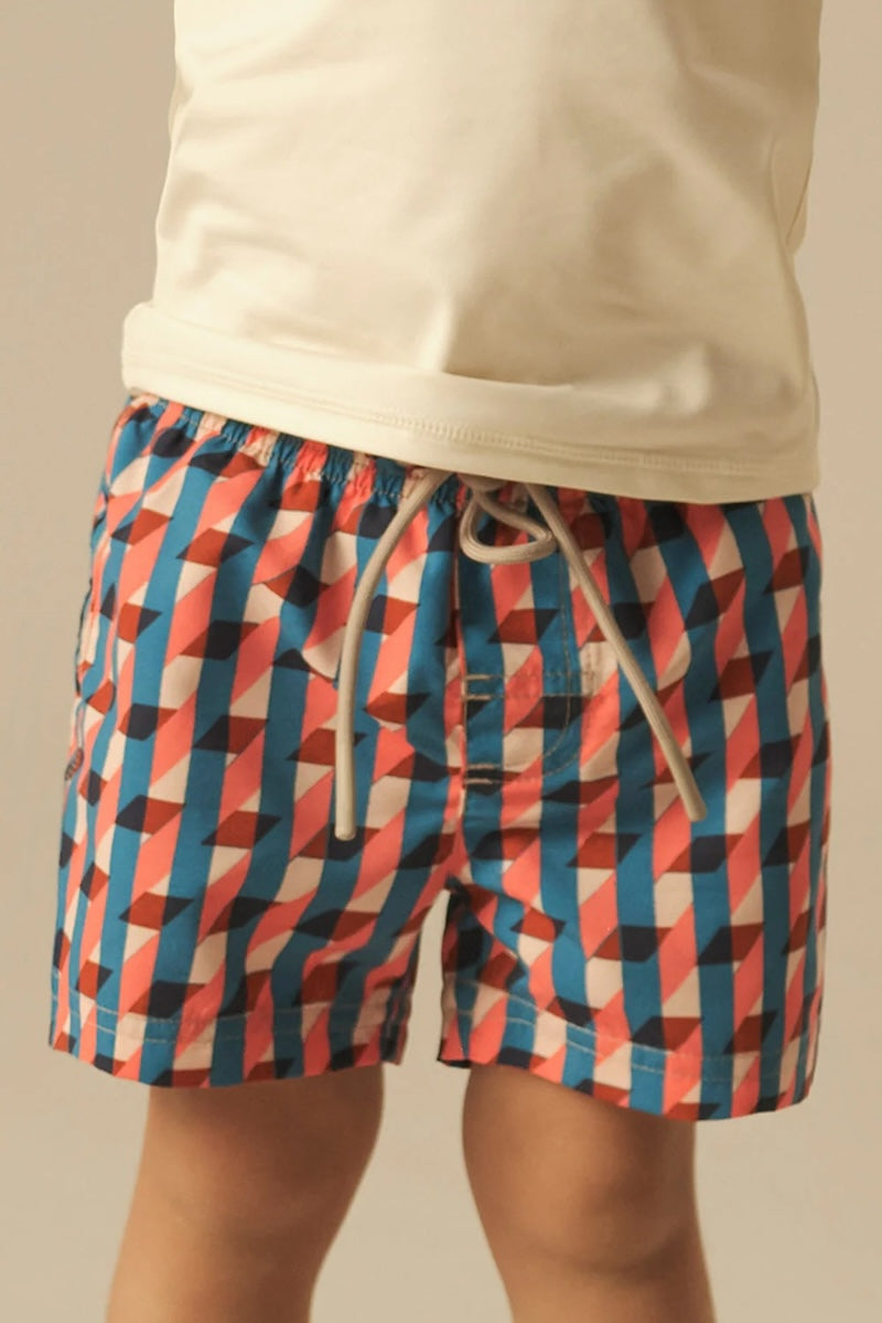 Colorful pink, red and blue geometric-patterned swim shorts worn by a person on a beige background.