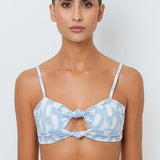 Woman wearing a light blue bikini top with a white geometric pattern on a plain background.