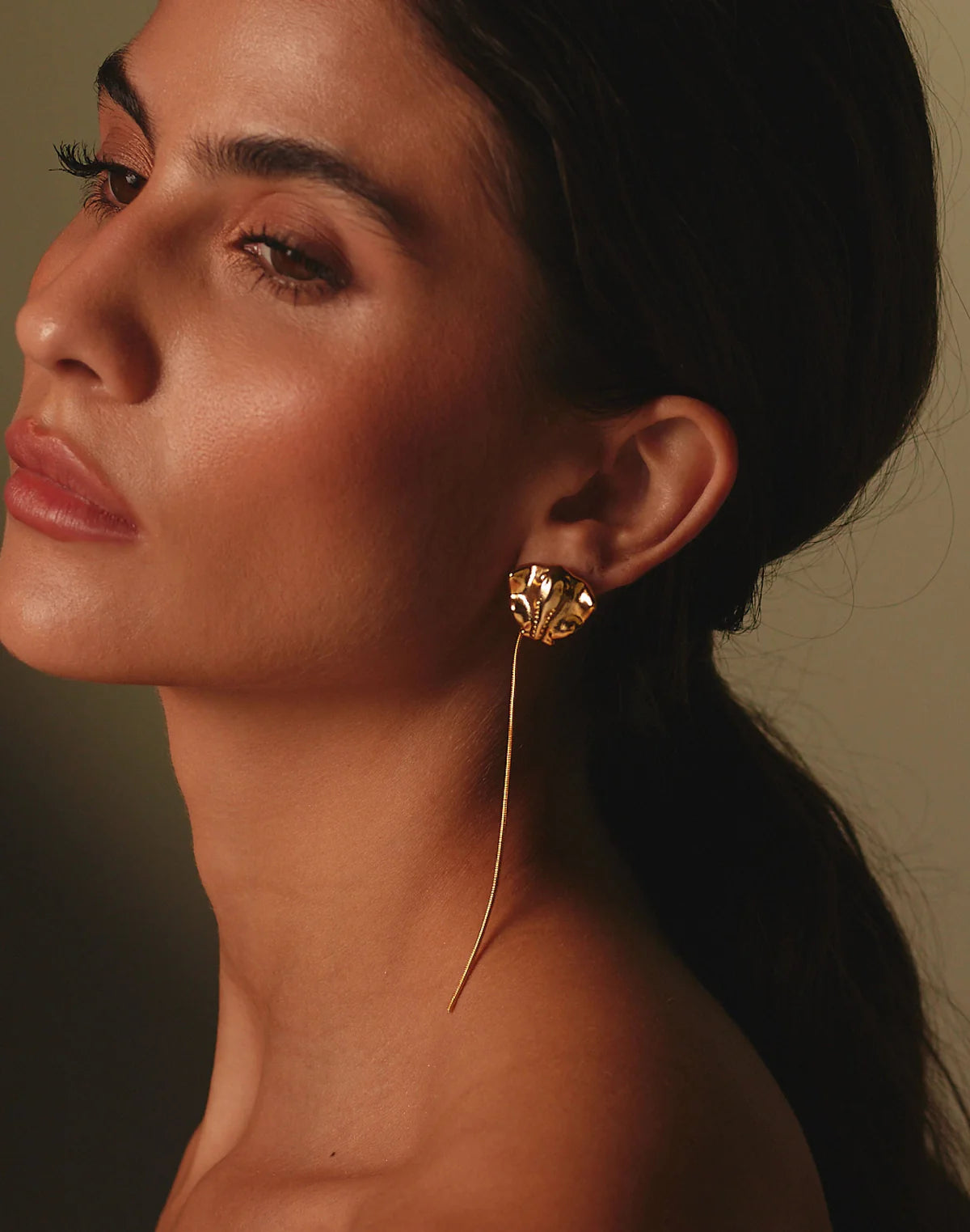 Close-up of a woman wearing a gold sting-ray earring with a dark background.