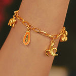 A close-up of a gold-plated charm bracelet on a person's wrist, featuring hand-painted charms.