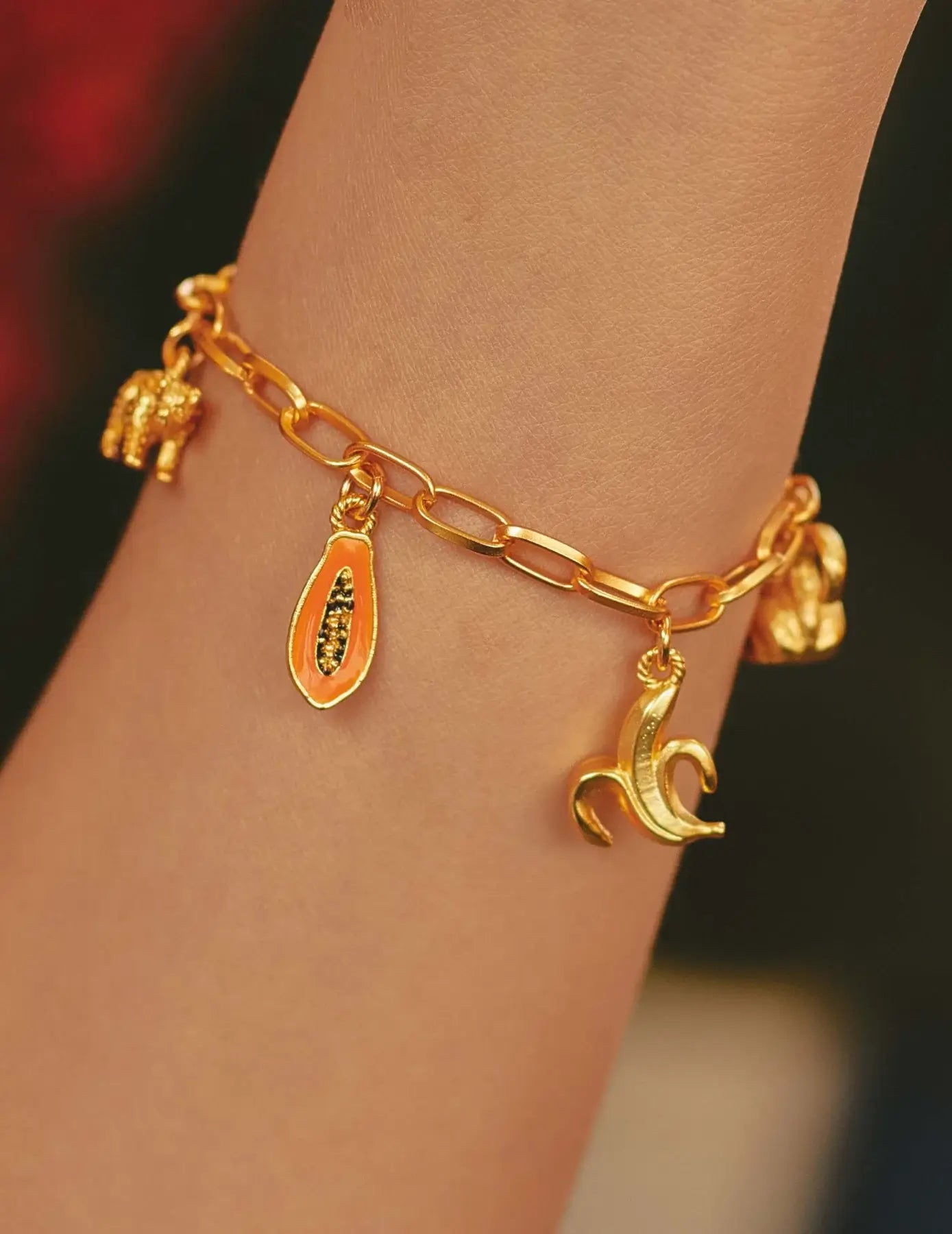 A close-up of a gold-plated charm bracelet on a person's wrist, featuring hand-painted charms.